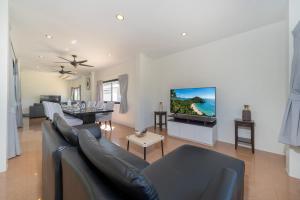 a living room with a couch and a tv on a wall at Rawai 3BR Villa Shared Pool near Shops & Dining in Ban Saiyuan (1)