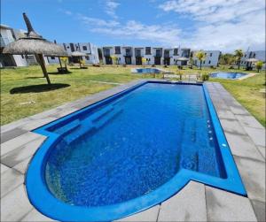 a blue swimming pool with an umbrella and a building at Duplex Green Village in Grande Gaube