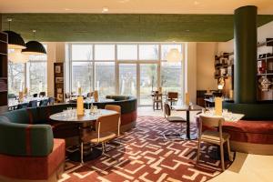 a restaurant with couches and tables and windows at Hampton by Hilton Bordeaux Merignac Airport in Mérignac