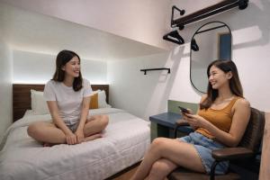 two women sitting on a bed looking at their cell phone at Faloe Hostel in Kota Kinabalu