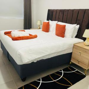 a large bed with orange and white pillows on it at 219 Contours Luxury Apartment in Victoria Falls +2 photos