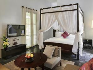 a bedroom with a canopy bed with a table and a couch at Sofitel Luang Prabang in Luang Prabang