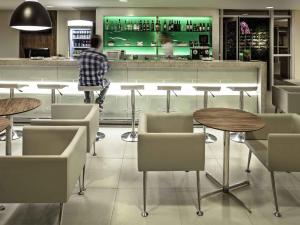 a man standing at a bar with tables and chairs at ibis Rio de Janeiro Parque Olimpico in Rio de Janeiro