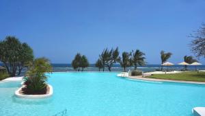 a large swimming pool with palm trees and the ocean at Zahari Oceanfront in Msambweni