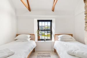 two beds in a white room with a window at Cosy Nook at Jam Jar Kitchen in Crantock