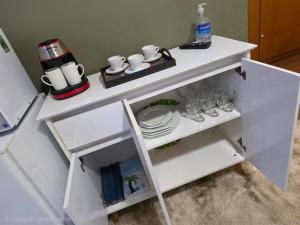 a white table with cups and glasses on a shelf at Flat 108B com lazer próx ao centro in Serra Negra