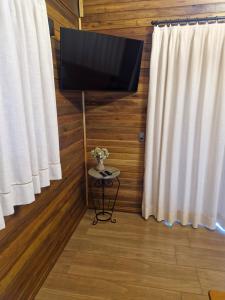 a flat screen tv on a wall next to curtains at Cabana Davos in Timbe do Sul