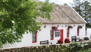 a white building with a thatched roof and red windows at Tourmakeady Self Catering in Toormakeady