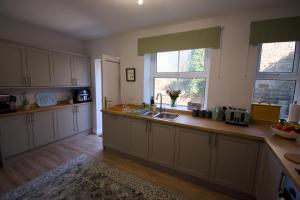 a kitchen with white cabinets and a sink and two windows at New! Luxury 4 Bedroom Detached House - Central Baslow in Baslow