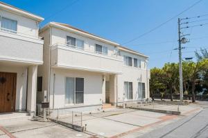 a white building with a balcony on a street at 照間Terumaの美しい海と太陽 Soleが目前に広がる和室ありの宿 TERUSOLEテルソーレ in Uruma