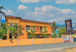 an orange building with palm trees in front of a street at R&B Guest House in Jaffna
