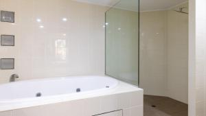 a white bathroom with a tub and a glass shower at Waterline Direct Poolside Apartment in Agnes Water