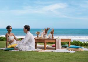 a man and woman sitting at a picnic table on the beach at Bali Beach Glamping in Tabanan