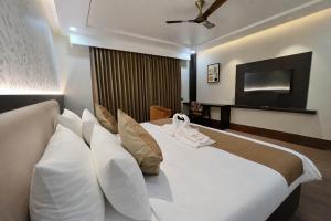 a bedroom with a large white bed with a flat screen tv at Hotel Mango Groves in Kotdwāra +17 photos