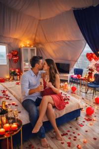 a man and woman sitting on a bed kissing at Sun Garden Glamping Domes in Călimăneşti +30 photos