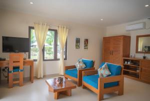 a living room with blue chairs and a television at Villas de Mer in Grand'Anse Praslin