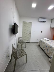 a bedroom with a bed and two chairs and a television at Studio perfeito para trabalho, concurso ou compras in João Pessoa