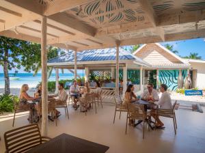 a group of people sitting at tables on the beach at Villas de Mer in Grand'Anse Praslin