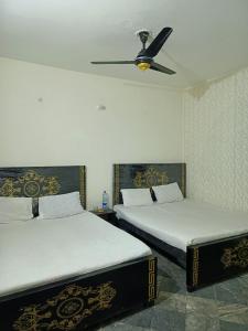 two beds in a bedroom with a ceiling fan at Al Shahzan Hotel in Lahore
