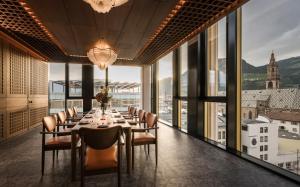 a dining room with a table and chairs and windows at Falkensteiner Hotel Bozen WaltherPark in Bolzano