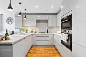 a white kitchen with white cabinets and a wooden floor at 'Bright Gem by the Sea' Premium Central 2 bedroom flat in Brighton & Hove
