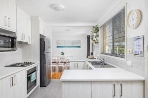 a kitchen with white cabinets and a large window at Barefoot Bungalow in Nelson Bay