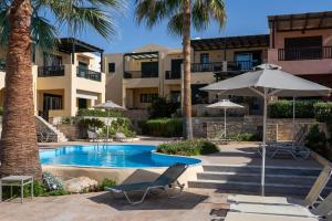 a resort with a swimming pool with chairs and an umbrella at Villa Avra in Panormos Rethymno