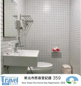 a white tiled bathroom with a sink and a toilet at Shan Cheng Guesthouse in Ruifang
