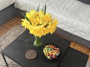 a vase with yellow flowers on a table next to a cake at Apartman Amal II in Vukovar