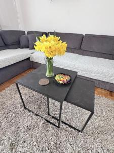 a black coffee table with a vase of yellow flowers at Apartman Amal II in Vukovar