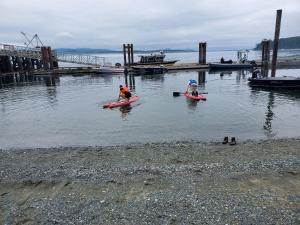 two people on kayaks in the water near a dock at The Orca Inn in Alert Bay