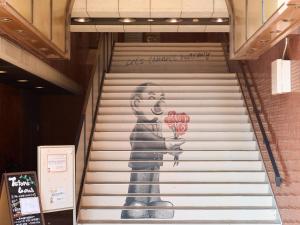 a staircase with a painting of a woman holding apples at Tabist Hotel Tetora Kitakyushu in Kitakyushu
