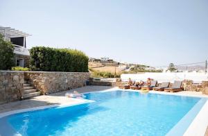a swimming pool with people sitting on chairs next to a house at Villa Magenta in Mikonos
