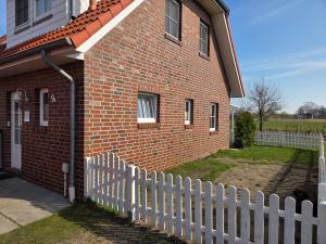 a red brick house with a white picket fence at Ferienhaus Seemöwe mit Deichblick Butjadingen-Burhave in Burhave
