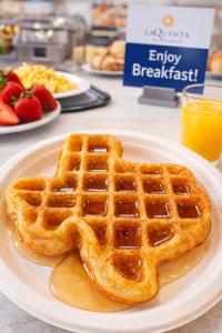 a plate of waffles with syrup and strawberries on a table at La Quinta by Wyndham Kerrville in Kerrville