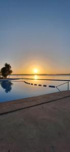 a pool with the sun setting in the horizon at GyC Laguna Resort in Chascomús