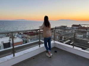 a woman standing on a balcony looking out at the ocean at Villa Maria Apartments by BookVillaEU in Nea Kallikrateia