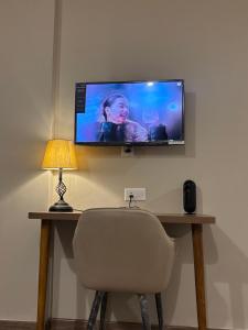 a television on a wall above a desk with a chair at Aarcos Stays in Greater Noida