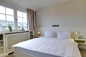 a white bedroom with a large white bed and windows at Friesenjung in Wenningstedt