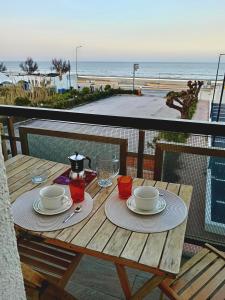 a wooden table with plates and glasses on a balcony with the beach at Suite Fronte Mare Senigallia- Terrazza Esclusiva sulla Spiaggia in Senigallia