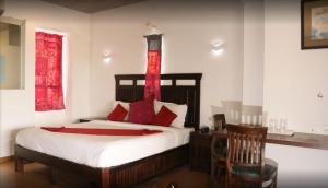 1 dormitorio con cama con almohadas rojas y escritorio en Hotel Zorba Inn, en Kolhapur