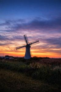 a windmill in a field with a sunset in the background at Thurnefield Holiday Cottages in Potter Heigham