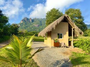 a small hut with a thatched roof with a mountain in the background at Redstone Cottage Gal Oya in Galgamuwa