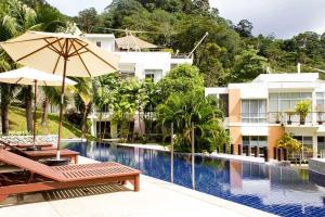 a pool with two chairs and an umbrella next to a building at Kamala Hills Serviced Apartments in Kamala Beach