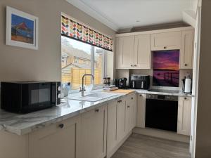 a kitchen with white cabinets and a sink and a window at Palm Tree House in Filey