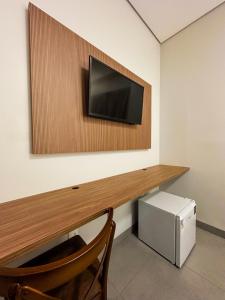 a room with a desk with a television on a wall at Hotel Essência Campo Erê in Campo Erê