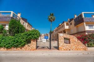 a stone wall next to a building with a palm tree at SiCasa Punta Prima in Punta Prima