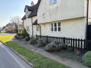 a white house with a fence next to a street at Charming Detached Cottage Guest Room in Silsoe Village in Bedford