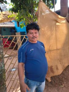 a man in a blue shirt standing next to a tree at Cookiewalla in Arambol
