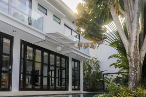 a white building with black windows and a tree at The Lavana Dzawani Villa Berawa Kuta Bali 3 Bedroom Villa in Canggu